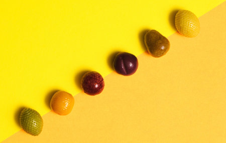 Arrangement of marzipan fruit shaped candies in different colors and shapes - lemon, plum, orange, apple against diagonal of yellow and orange background. Taken from above.の写真素材