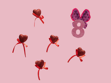 International Women's Day (8th March) concept. Pink glitter number eight with wings with five red hearts flying on pastel pink background.の写真素材