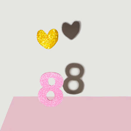 International Women's Day (8th March) concept. Pink glitter number eight with heart shaped natural leaf colored in gold with shadow on gray background.の写真素材