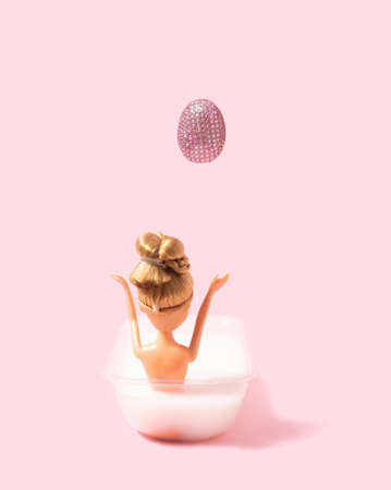 A girl doll in bathtub enjoying life. Sparkling disco egg. Pastel pink background.の写真素材