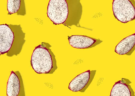 Pattern created from fresh exotic dragon fruit halves, slices and seeds on bright yellow background....