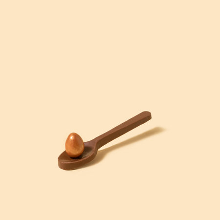 Chocolate spoon with small chocolate golden color egg concept. Beige background.の写真素材