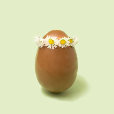 Big chocolate egg with daisy chain headpiece minimal arrangement. Mint green background.の写真素材