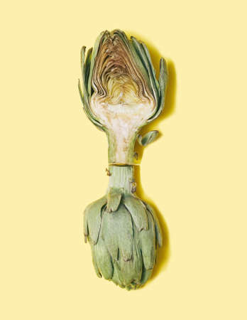 Lovely and delicious artichoke vertically aligned against pastel yellow background. Flat lay...