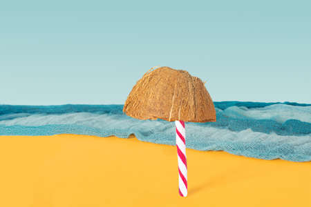 Beach with a lonely sun umbrella abstract concept. Candy cane and half of fresh raw organic coconut in front with blue ocean color scarf and blue sky background.の写真素材