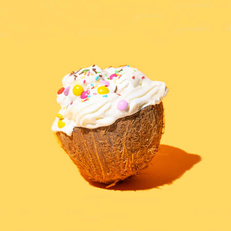 A half of fresh raw organic coconut filled with white sweet whipped cream with colorful decoration on the top. Warm orange background.の写真素材