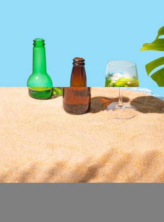 Two beer bottles and a cocktail glass with fresh mojito on the sandy beach with palm leaf shadow, and natural monstera on side. concept for vacation.の写真素材