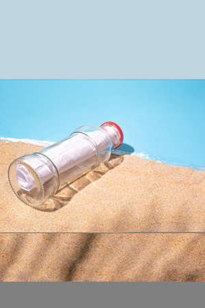 Letter message in a glass transparent bottle on the sandy beach with palm leaf shadow, concept for...