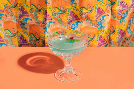 One deluxe crystal glasses with magic green cocktails and cornelian cherry in it.  Unique silk and orange background.の写真素材