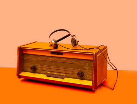 An antique radio with old type of headphones. Retro vibe arrangement against light orange and light orange background.の写真素材