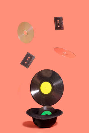 EP, LP vinyl records, cd and cassette tape popping out of traditional black bowlers hat. Funky minimal concept made on terracotta background.の写真素材