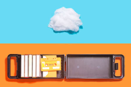 Past and present music inspired concept. Open box with cassette and cotton cloud shaped prop against blue and terracotta background.の写真素材