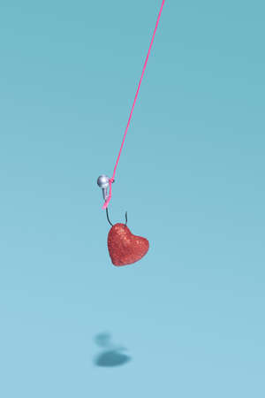 Hooked red shiny heart hanging on pink thread on a blue background with shadow