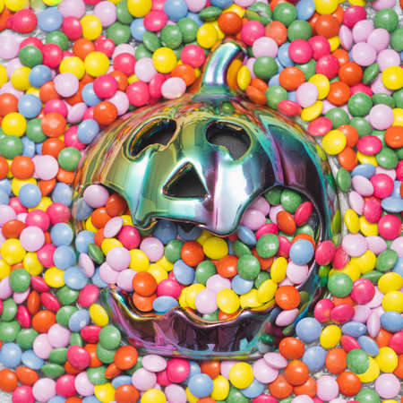 Cyberpunk halloween neon pumpkin floating almost fully covered with a lot colorful small chocolate bonbonsの写真素材