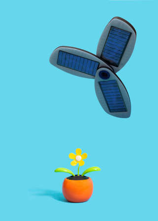 Solar power and renewable energy inspired concept. Small portable solar panels above artificial yellow flower with small solar cell within against blue backgroundの写真素材