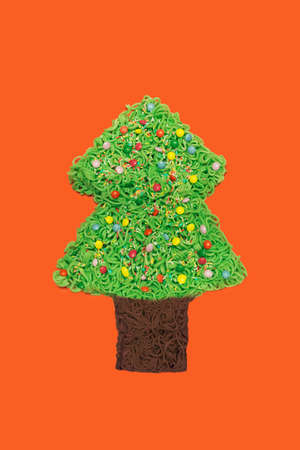 Festive eating concept. Noodle tree plate with colorful little chocolates. Flat lay arrangement with red backgroundの写真素材