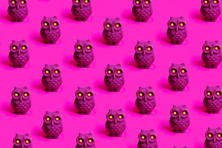 A pattern mad of little purple glitter owl toy with yellow eyes against vibrant magenta background.の写真素材