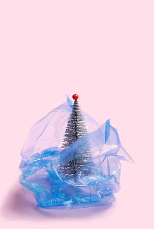 Environmentally issue inspired concept. Open plastic blue disposable blue bag. Glitter silver artificial Christmas tree with red berries. Creative copy space with baby pink backgroundの写真素材