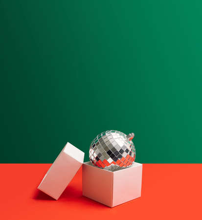 Festive inspired concept. Open gift disposable white box. Shiny disco ball inside it. Creative copy...