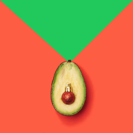 Christmas inspired minimal concept. Fresh half of avocado with shiny red christmas ball ornament against red and green background. Flat lay arrangement.の写真素材