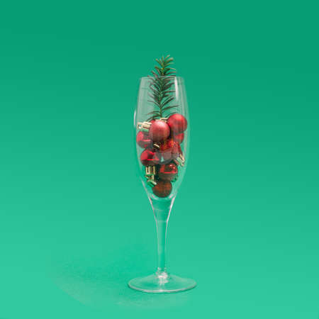 Unique christmas party concept. Champagne glass full of small red christmas ornament with green little spruce against lovely green backgroundの写真素材