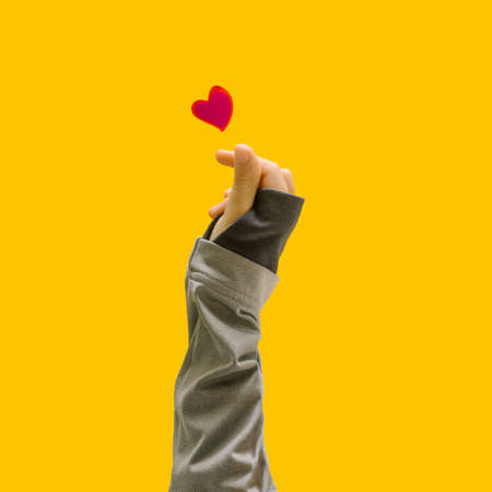 K pop concept. A girl teenager hand showing finger heart gesture. Red heart above. Unique yellow background.の写真素材