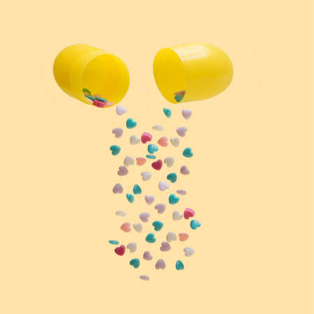 Love medicine minimal concept. Yellow capsule with laid out colorful heart shaped pills. Pastel yellow background.の写真素材
