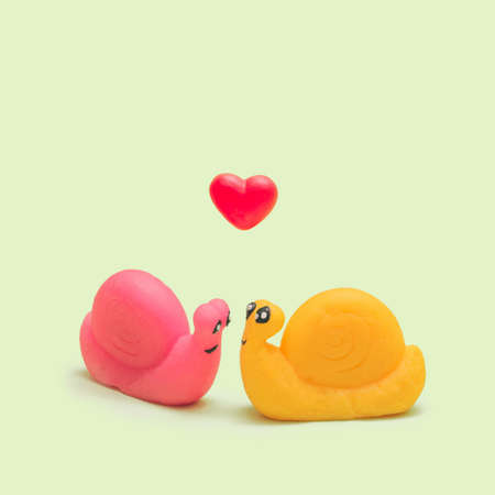 Couple in love concept. Pink and yellow soft snail toys close to each other with red heart jelly candy above it.Pastel lime green backgroundの写真素材