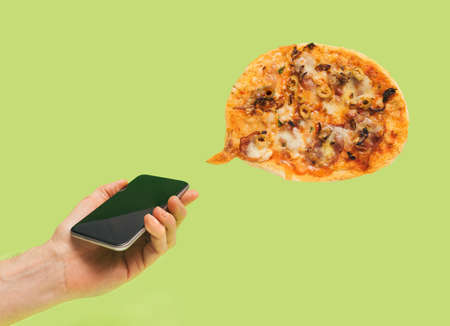 A male hand holding a mobile phone with pizza in the shape of speech bubble. Light green background.の写真素材