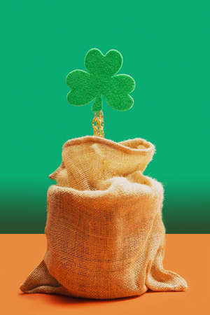 Abstract golden treasure minimal concept. Green shamrock taking a goldenÂ chain out of a treasure bag. Pastel green and terracottaÂ background.の写真素材