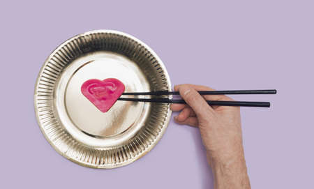 The man's hand holding black chopsticks with red yummy heart shaped ravioli golden shine plate...