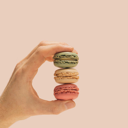 The man's hand holding green, beige and pink color attractive and yummy macaron . Champagne...