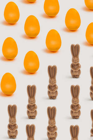 Easter optimistic pattern concept. Arrangement made with many delicious organic rabbit chocolates with a lot of funky yellow eggs. Pastel beige backgroundの写真素材