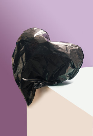 Broken heart concept. Black heart shaped balloon crashes on the edge of pink and champagne color surfaces. Very peri purple color in background.の写真素材