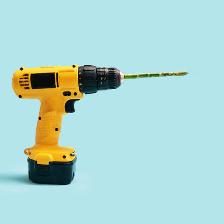 Vegan and vegetarian minimal concept. Yellow cordless drill with one fresh asparagus tip against a blue background.の写真素材