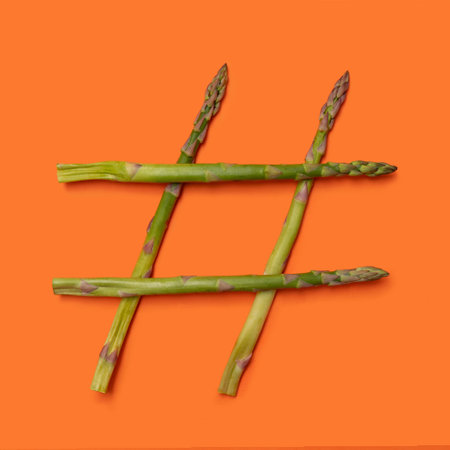 Social media, vegan and vegetarian minimal concept. Four fresh asparagus tips as a hashtag symbol against an orange background.の写真素材