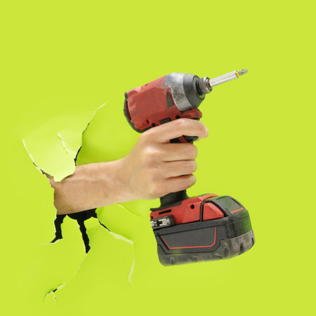 Man hand holds brushless cordless impact driver that breaks through bright green wallの写真素材