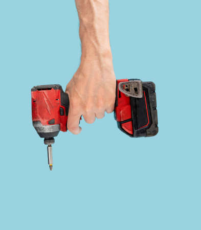 Man hand holds brushless cordless impact driver that comes from abobove on pastel blue background