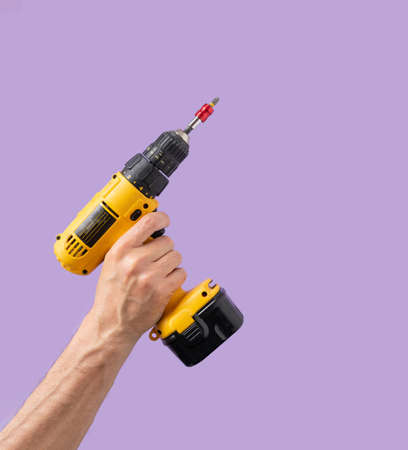 Man hand holds Brushless Cordless  Drill that comes from corner on purple color backgroundの写真素材