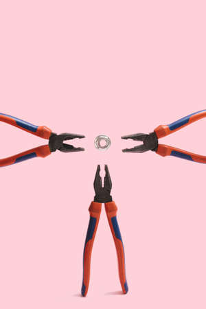 Three high leverage combination pliers from three directions around with hex nut in the middle on pink color backgroundの写真素材