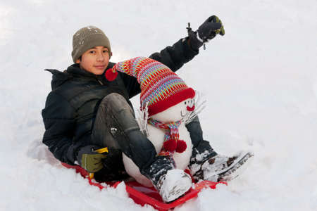 Boy with toboggan and snowmanの写真素材