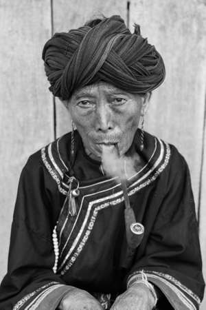 Phongsali Privince, Laos - 25.July 2010: senior adult hill tribe woman in traditional clothes smoke her pipeのeditorial素材
