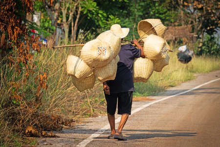 Sang Khom, Thailand - April 9, 2019: Old man of Thailand walk to the local market to sell his hand made basketsのeditorial素材