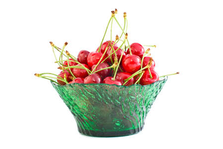 Green glass bowl filled with the red cherries isolated on the white backgroundの写真素材