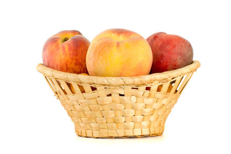 Three tasty peaches in wicker basket isolated on the white backgroundの写真素材