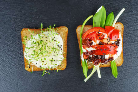 Green alfalfa sprouts,fresh and dried tomatoes on toasted slices of wholegrain bread on black stone...