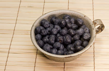 a tin cup full of blueberries on a bamboo placemat
