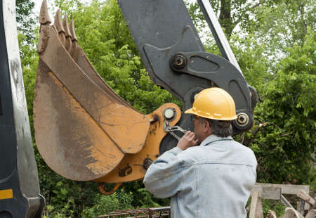 man changing a cotter pin on a large backhoe bucket