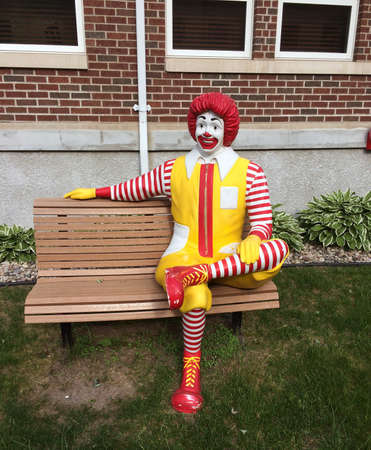 The Ronald McDonald mascot sitting on a bench in full makeup.のeditorial素材