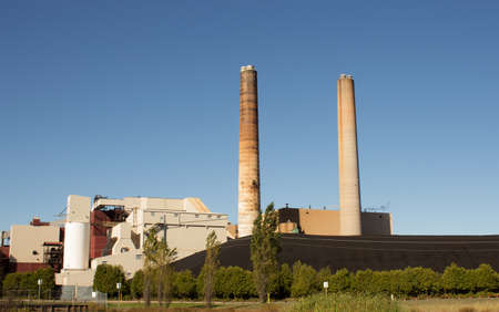 A large coal fired power plant with smoke stacks and coal pile.の写真素材